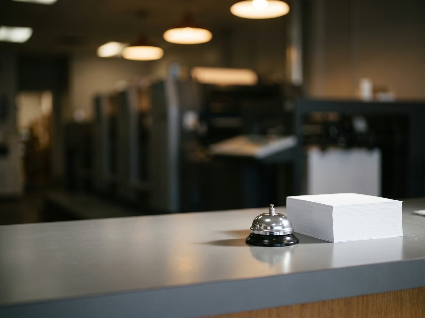 A print shop counter with a service bell and a stack of white paper
